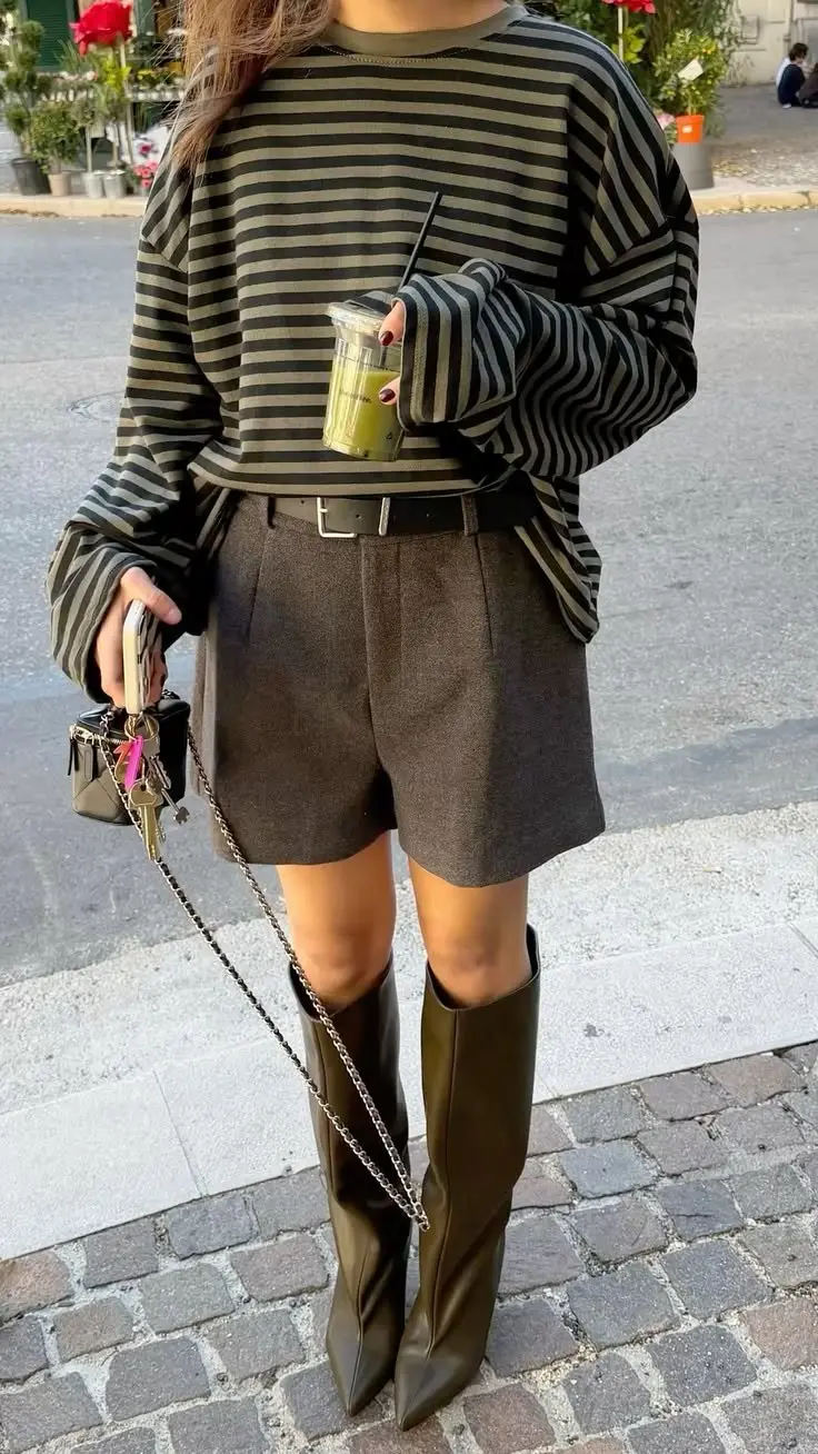 woman in olive black stripe oversized long sleeve tee dark charcoal high waist wool tailored shorts tall dark leather knee boots and small chain bag street style outfit 7