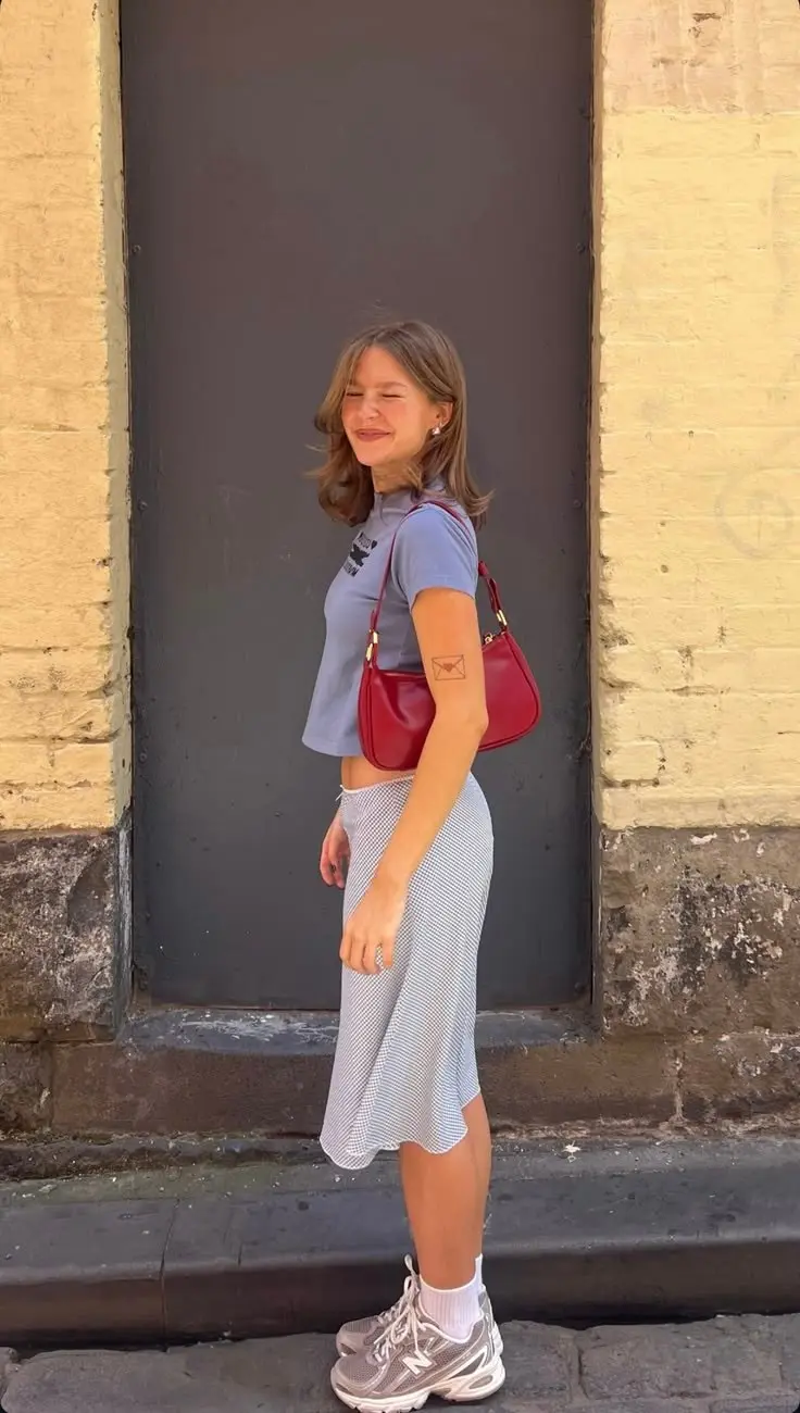 woman in blue baby graphic crop tee grey blue gingham midi bias skirt red shoulder bag white socks and grey New Balance chunky sneakers street style outfit 9