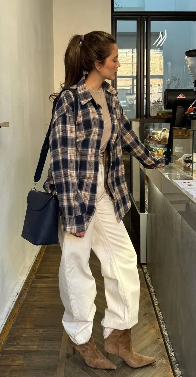 woman in navy cream pink plaid flannel open overshirt cream fitted tee white barrel leg jeans camel suede ankle boots and small navy crossbody bag at coffee shop outfit 10