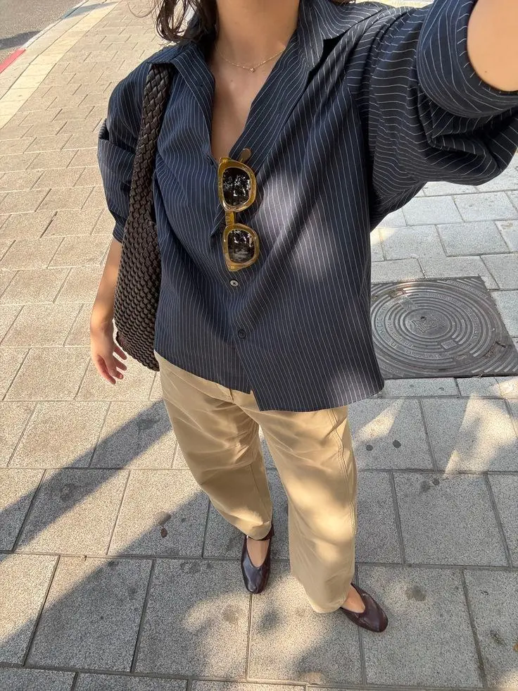 woman in dark navy pinstripe oversized button down shirt khaki wide leg trousers dark brown ballet flats tortoiseshell sunglasses and dark woven leather shoulder bag street selfie outfit 11