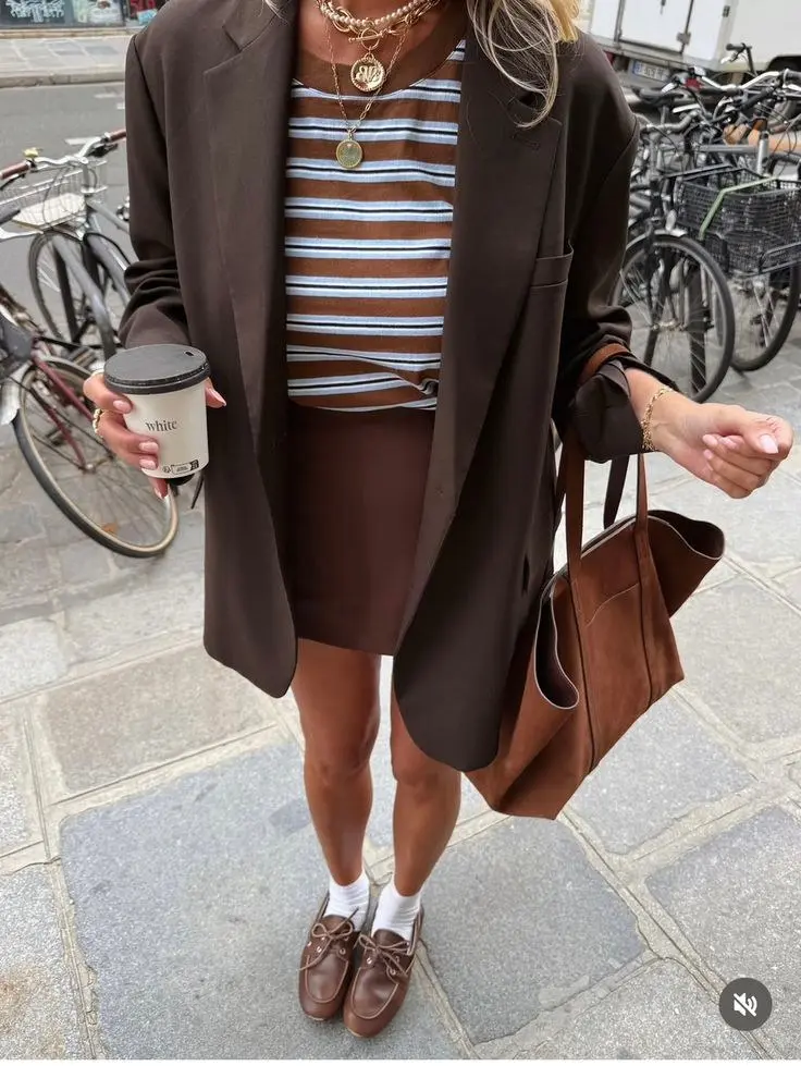 woman in oversized dark brown blazer brown white stripe crop tee brown mini skirt brown loafers white socks large caramel suede tote layered gold necklaces street style outfit 12