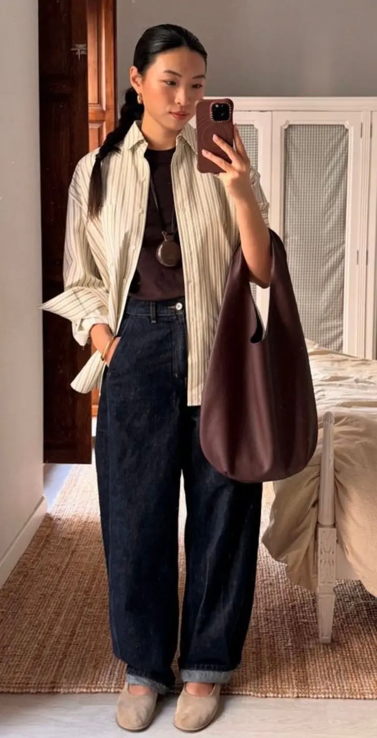 woman in cream stripe oversized button down shirt layered over dark brown fitted tee dark indigo barrel leg jeans beige ballet flats large oxblood leather hobo bag mirror selfie outfit 13