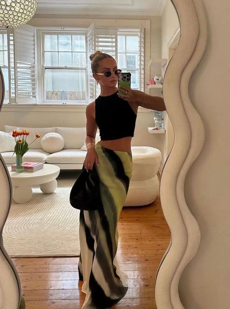 woman in black sleeveless crop top and olive black cream abstract print bias cut maxi skirt holding small black bag wearing small oval sunglasses mirror selfie outfit 13