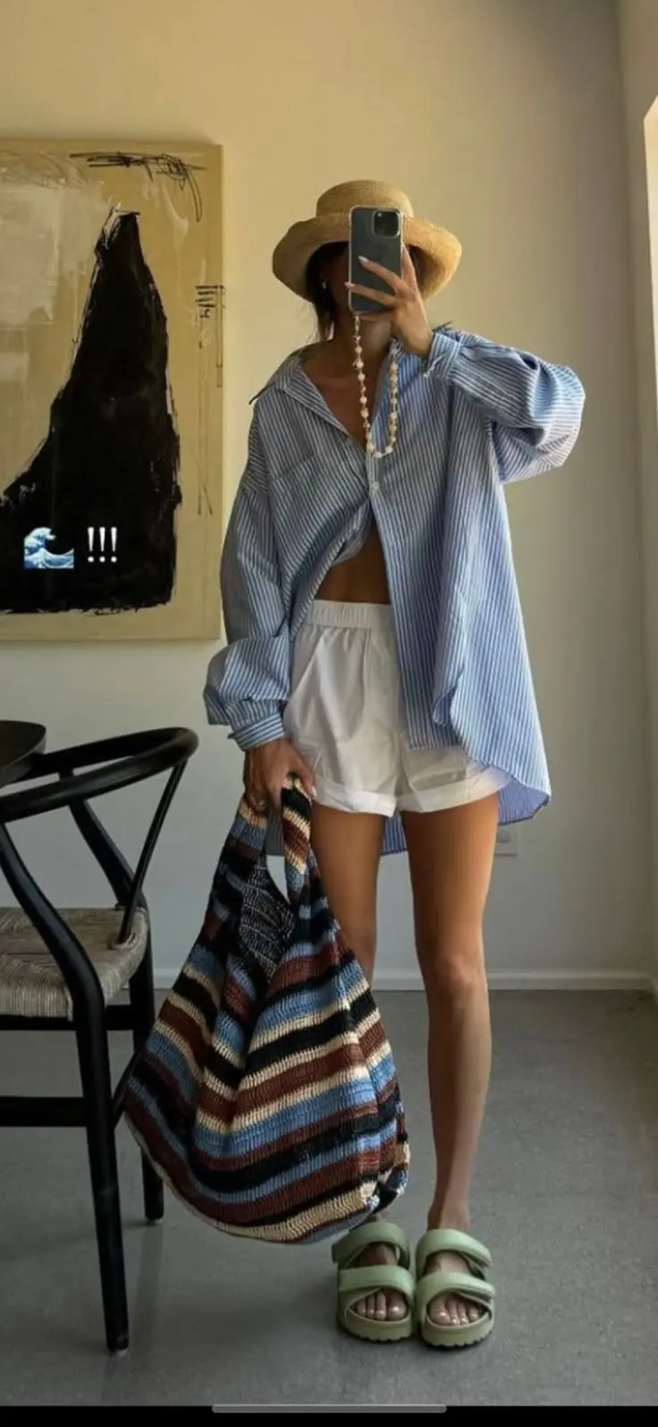 woman in oversized blue and white striped oversized shirt over white sports bra and white shorts with pearl layered necklace straw hat striped crochet tote bag and platform sandals mirror selfie outfit 15