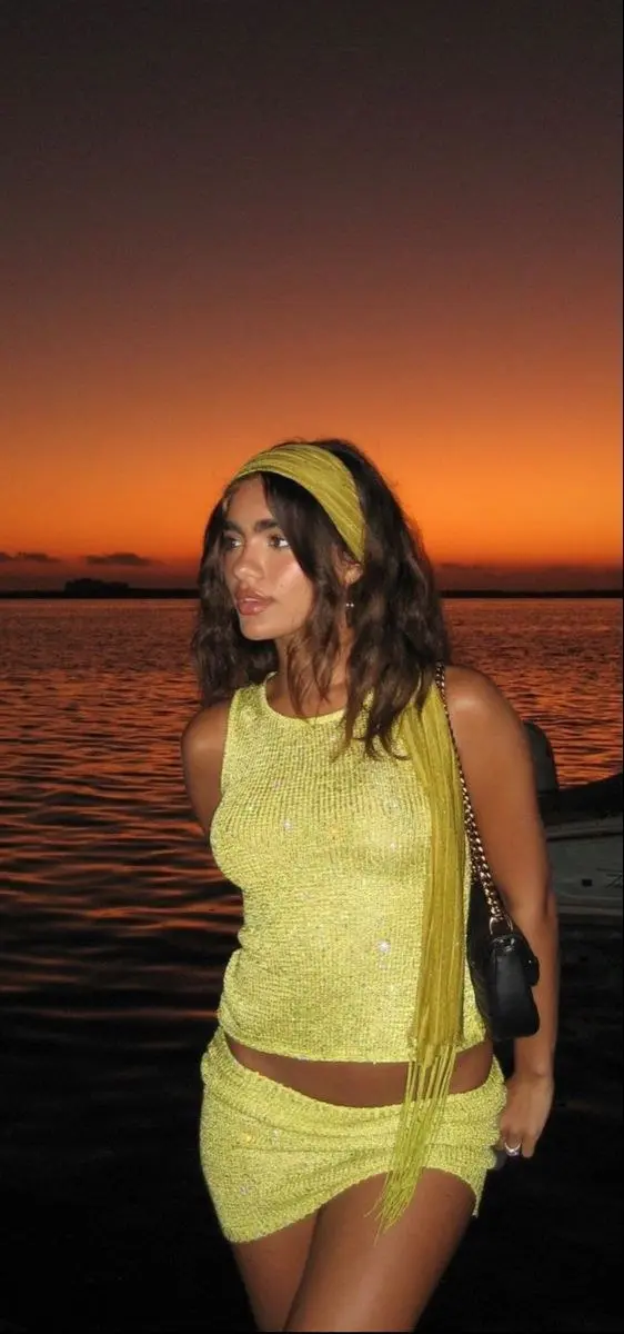 woman in lime yellow sequin ribbed knit crop tank and matching mini skirt with yellow fabric headband and small black chain shoulder bag at sunset over water outfit 17