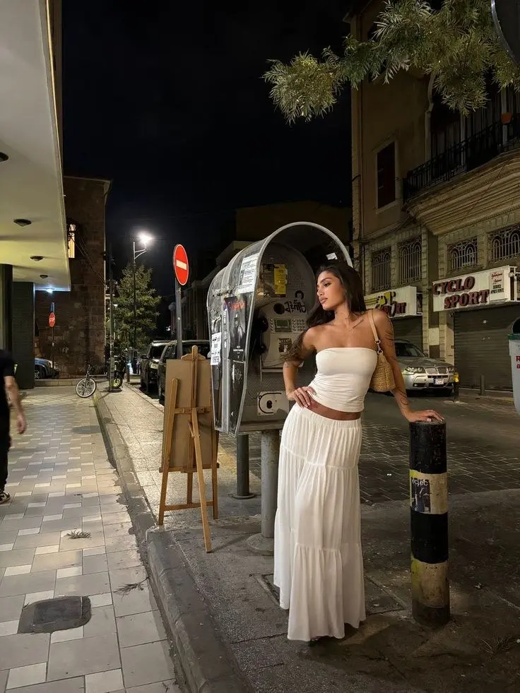 woman in white strapless tube top white tiered maxi skirt small rattan woven bag on city street at night outfit 3