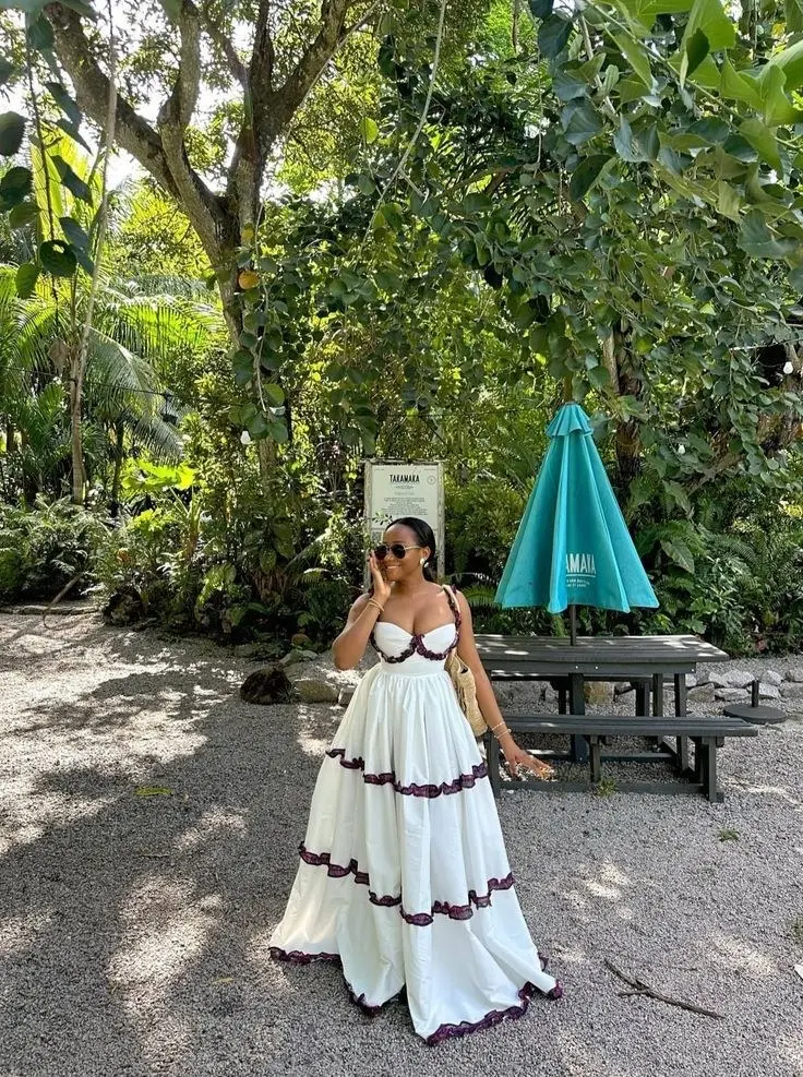 woman in white tiered maxi dress with dark berry lace trim corset bodice straw bag sunglasses in tropical garden setting outfit 4