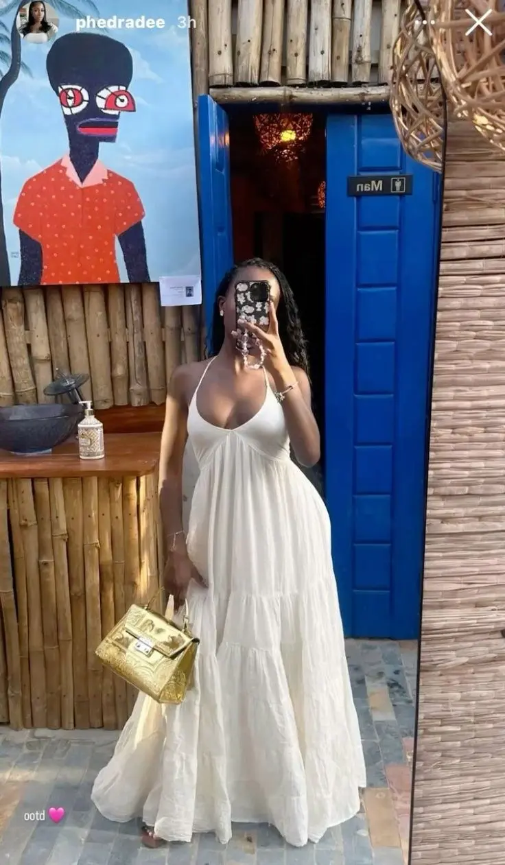 woman in white halter neck tiered maxi dress gold structured handbag flower phone case mirror selfie at boho restaurant bamboo wall blue door outfit 5