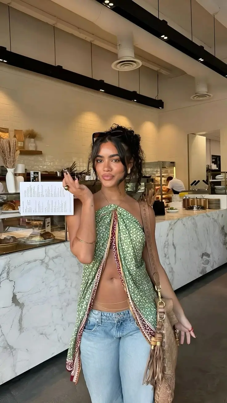 woman in green printed scarf wrap top light wash jeans tan leather crossbody bag gold jewelry at marble counter café outfit 6