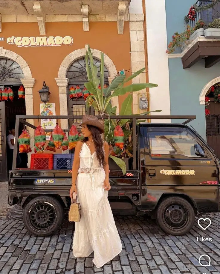 woman in white cotton maxi dress with lace crochet inset detail wide brim cognac cowboy hat small woven bag standing on cobblestone street colorful building truck behind outfit 15