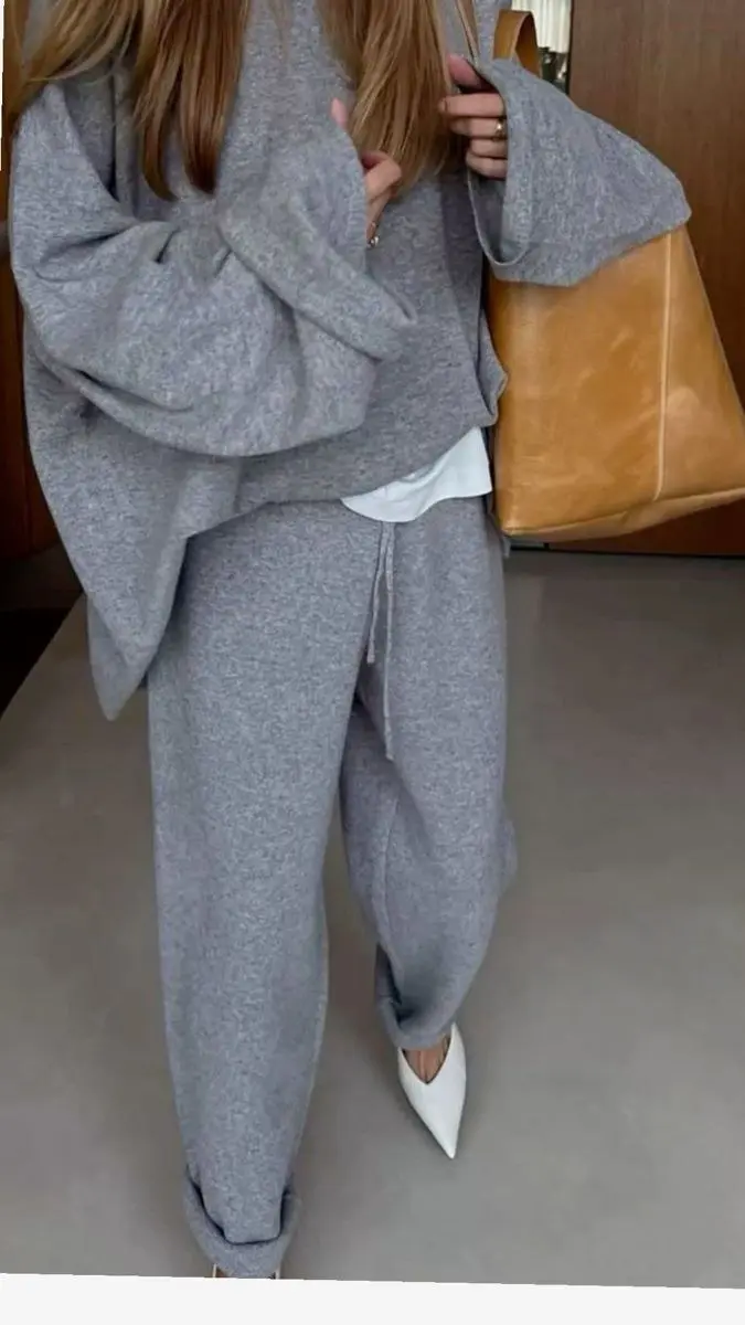 Matching gray knit set — relaxed sweater and wide-leg pants — styled with black Mary Jane flats and a single gold chain, editorial street style