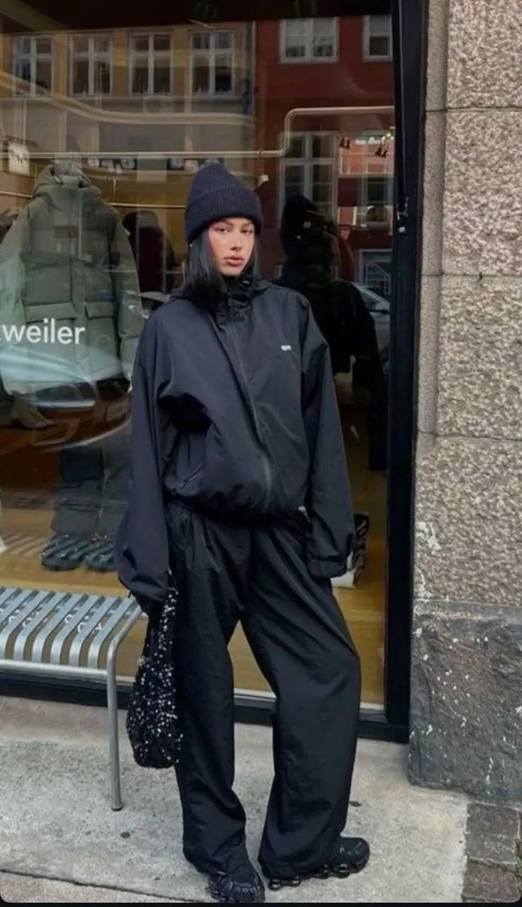 Sleek matte black technical raincoat over camel suit trousers and a thin knit, minimalist gorpcore street style