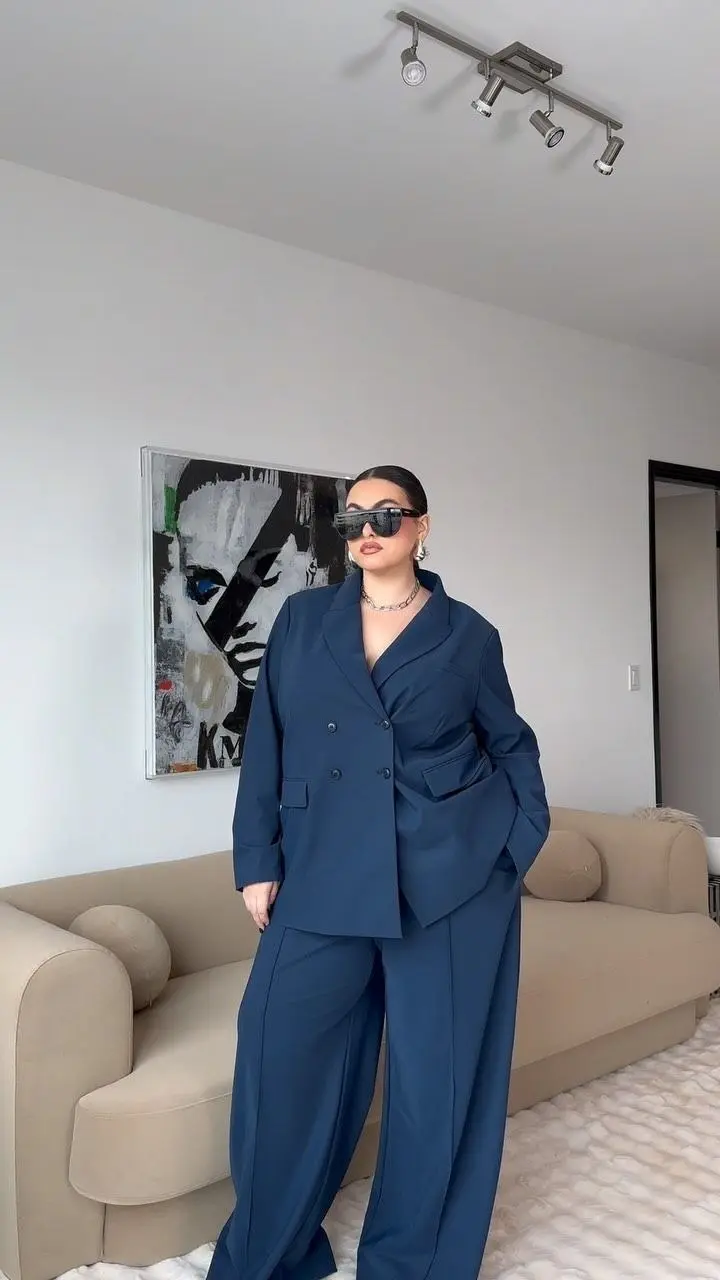 Stylish curvy woman in emerald green structured blazer, matching trousers as a suit, gold jewelry, editorial indoor lighting