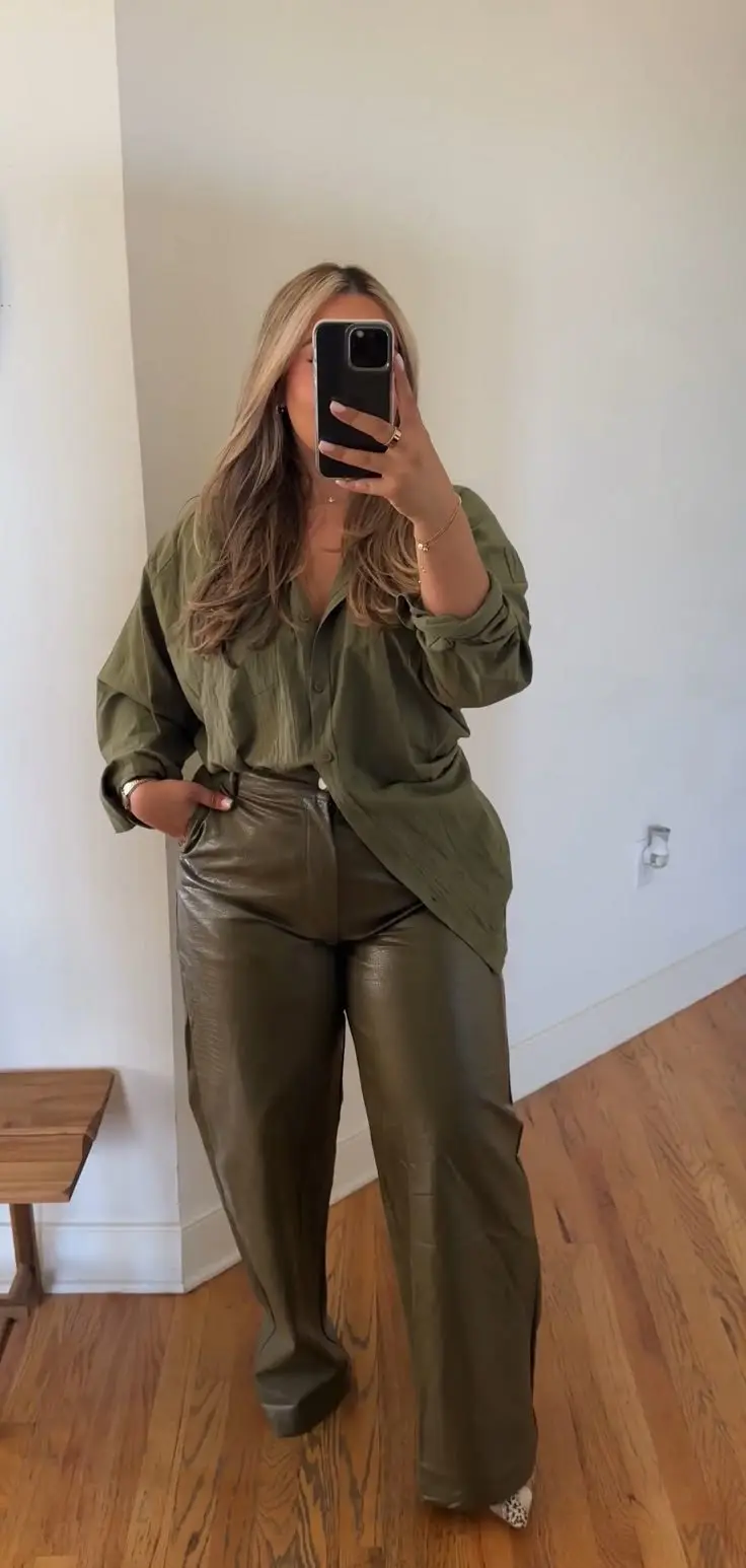 Stylish curvy woman in black leather wide-leg trousers, satin blouse tucked in, pointed toe heels, indoor setting