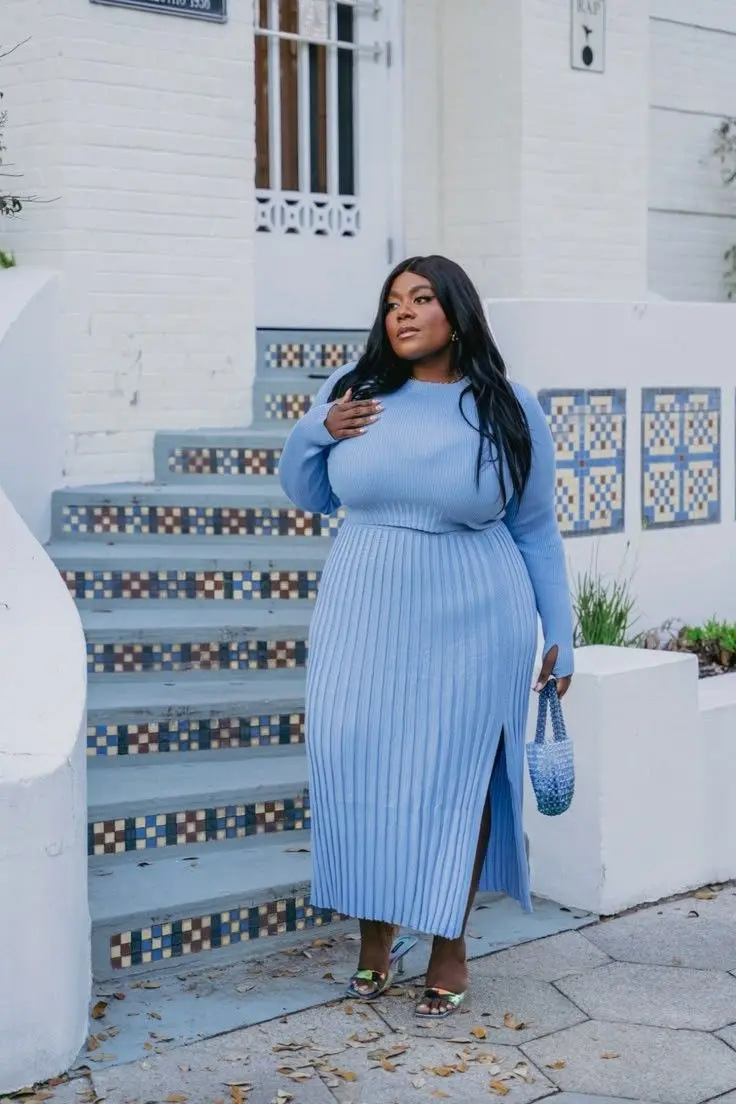 Plus size woman in jewel-tone teal satin blouse, black high-waist wide-leg trousers, pointed toe heels, indoor cafe setting