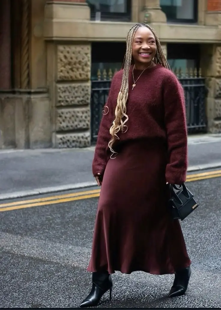 Editorial shot: curvy model in deep plum velvet midi dress, black ankle boots, autumn foliage background