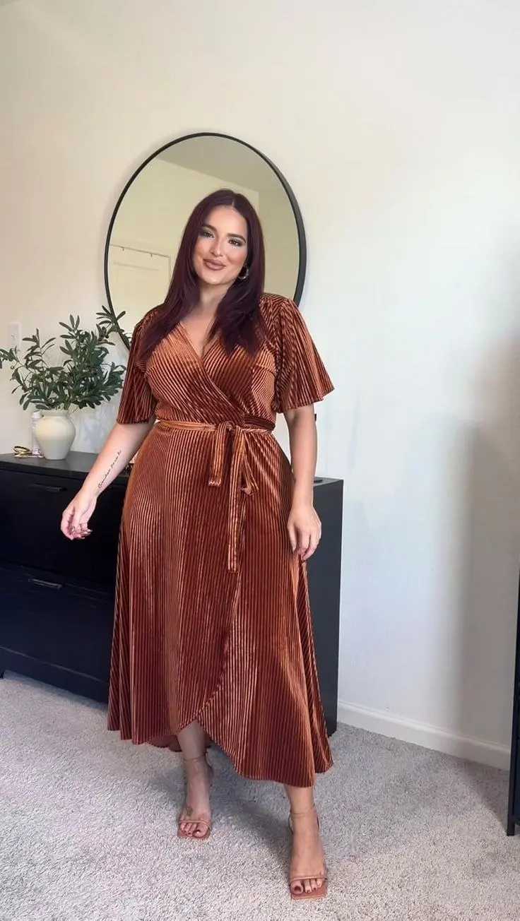 Curvy woman in leopard print wrap midi dress, knee-high black boots, gold hoop earrings, fall city setting