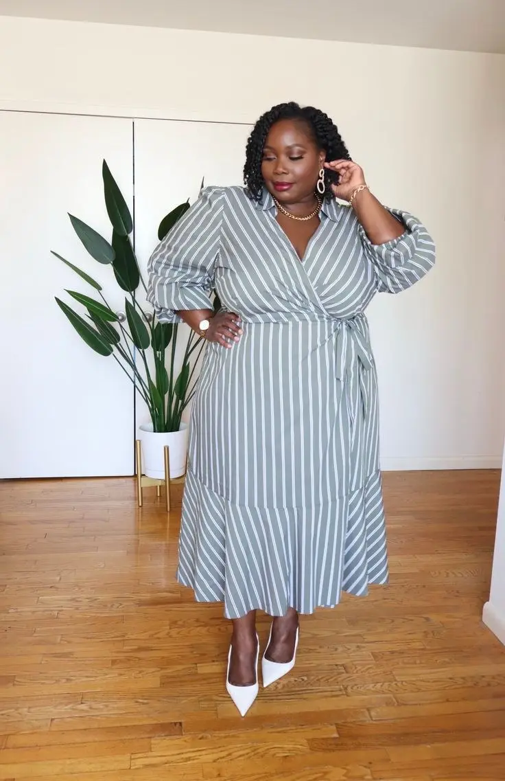 Plus size woman in black matte jersey wrap dress, pointed kitten heels, red bag statement accessory, minimal and chic