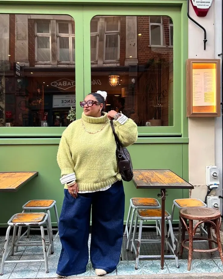 Stylish curvy woman in rust orange voluminous knit, high-waist wide-leg black trousers, gold jewelry, city sidewalk