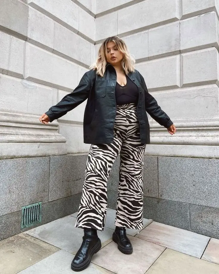 Editorial shot: curvy model in cheetah print midi dress worn with a belt, brown knee-high boots, natural fall lighting