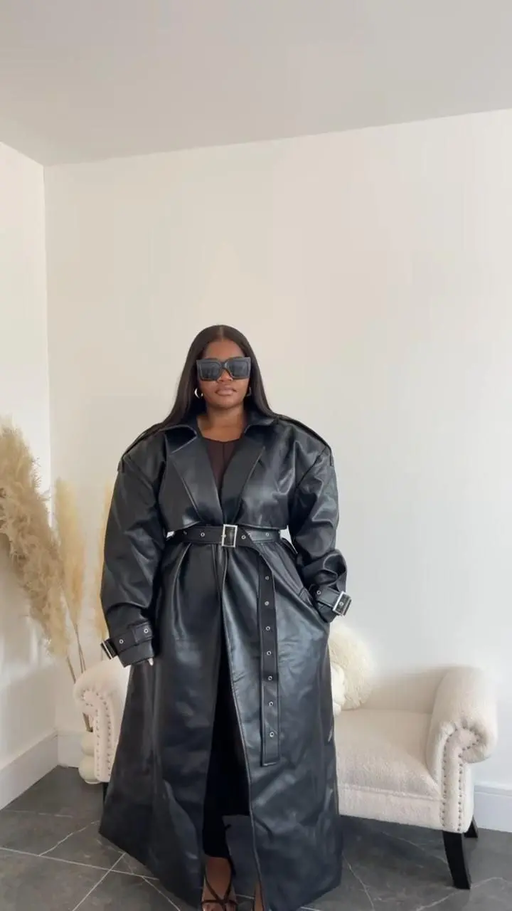 Plus size model in deep forest green longline coat, black wide-leg trousers, pointed ankle boots, editorial fall lighting
