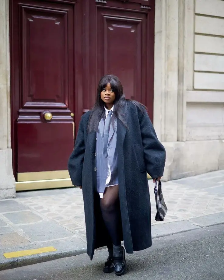 Stylish curvy woman in charcoal grey longline structured coat, ribbed turtleneck underneath, gold jewelry, city setting