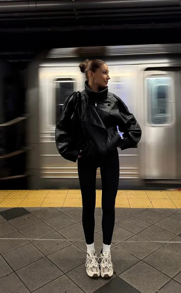 woman in black oversized leather jacket black leggings white New Balance sneakers white ankle socks bun hairstyle subway platform outfit 1