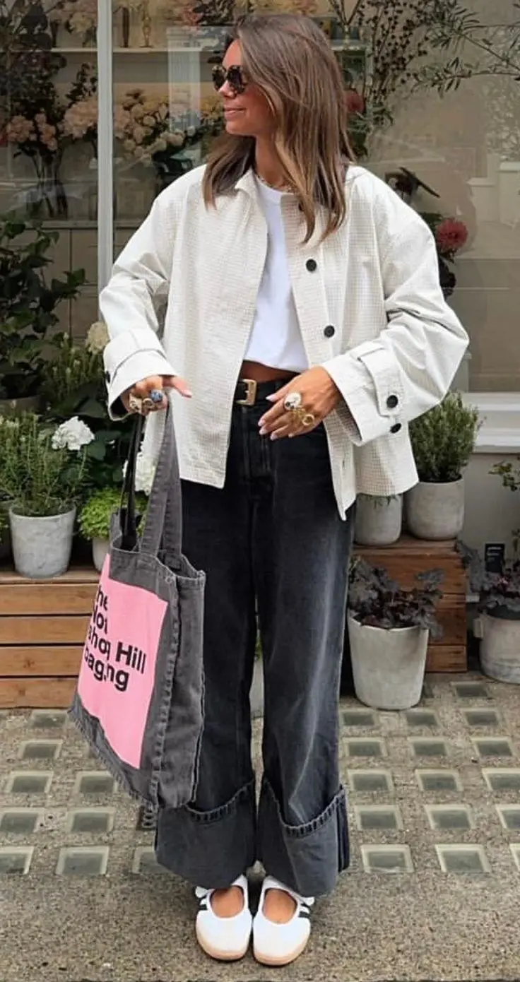 woman in ivory overshirt open over cropped white tee dark grey wide-leg jeans white sneakers sunglasses statement rings large grey denim graphic tote bag outdoor flower shop outfit 13