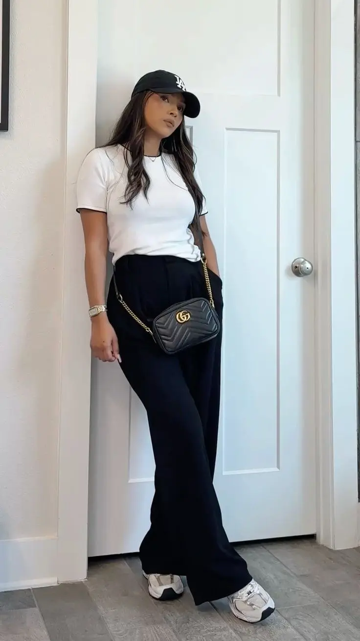 woman wearing black LA baseball cap white fitted ribbed tee wide-leg black trousers Gucci chain crossbody bag white New Balance sneakers indoor home outfit 18