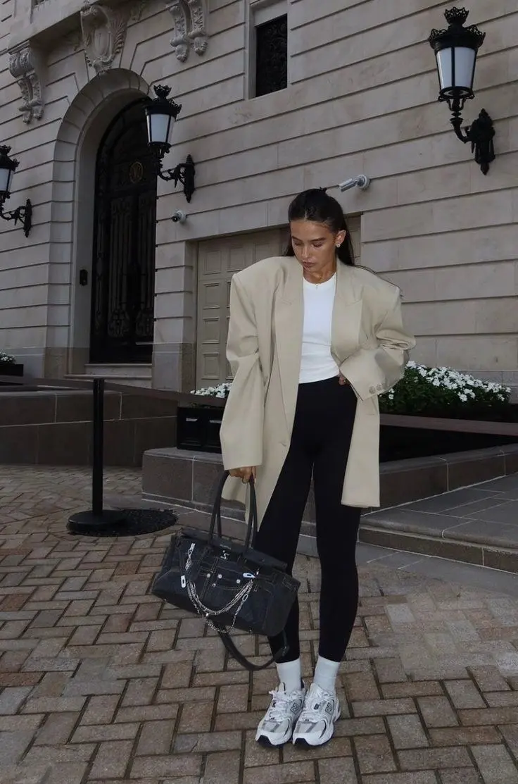 woman wearing oversized camel longline blazer white fitted tee black leggings white chunky sneakers white ankle socks large dark structured tote bag pearl earrings ponytail street outfit 19