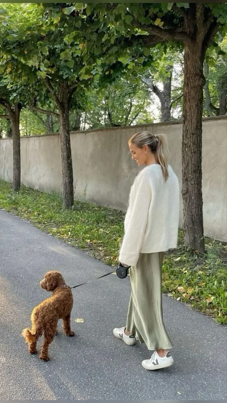 woman in cream oversized knit sweater sage green satin wide leg trousers and white Veja sneakers walking outdoors outfit 1