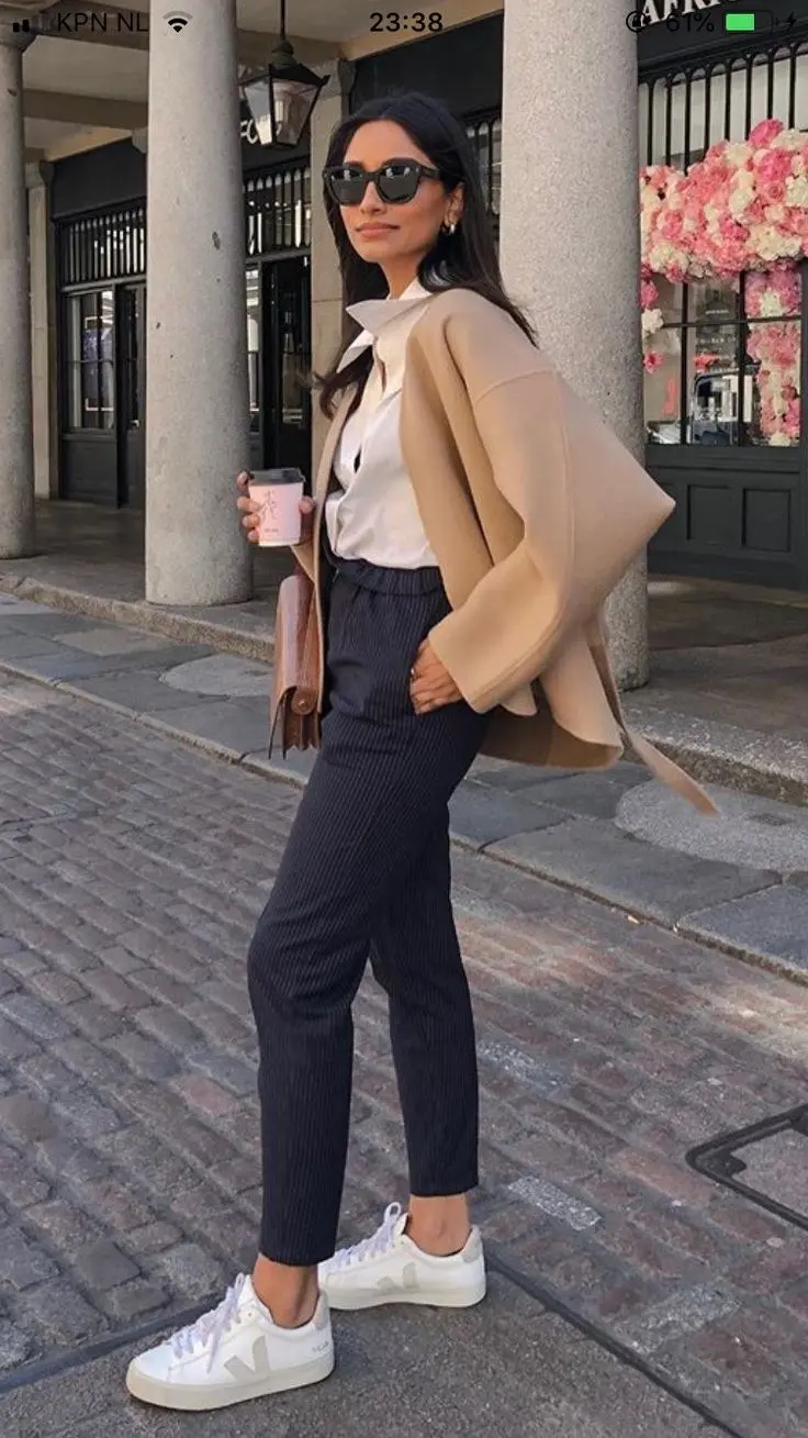 woman in navy pinstripe trousers white shirt camel blazer and white Veja sneakers holding coffee cup outfit 2