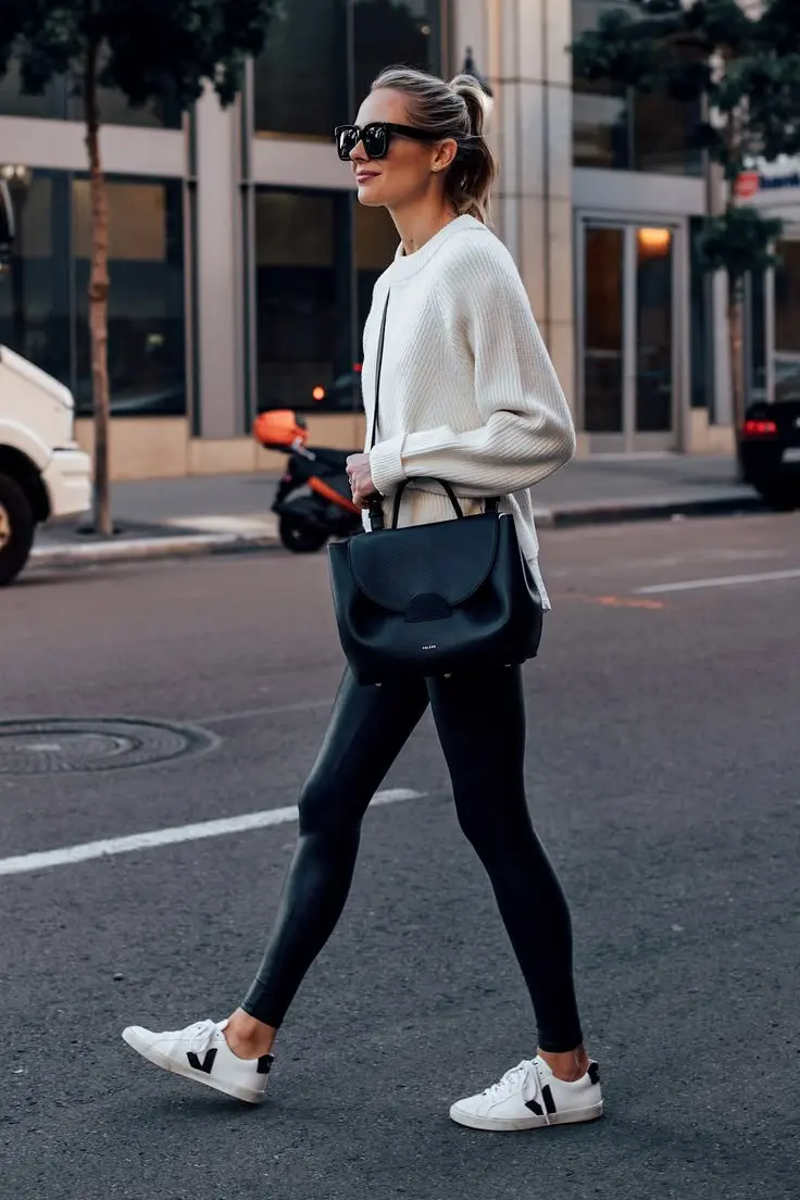 woman in oversized cream knit sweater black faux leather leggings black structured tote bag and white Veja sneakers crossing street outfit 6
