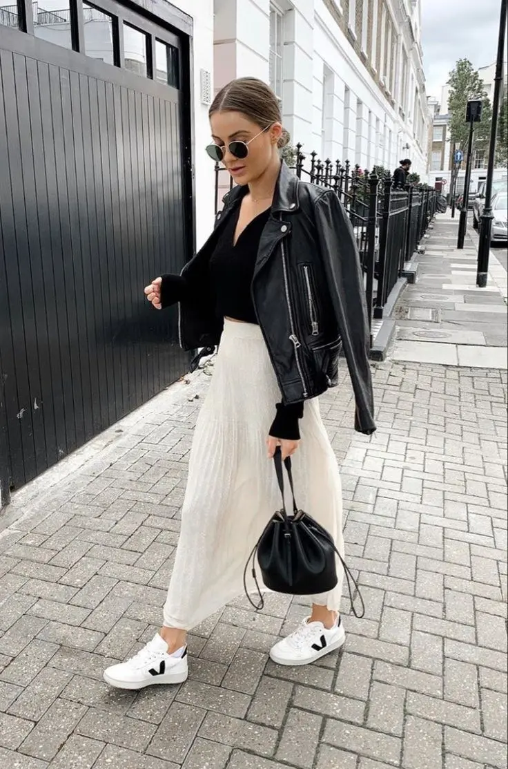 woman in black leather moto jacket black bodysuit cream pleated maxi skirt black bucket bag round sunglasses and white Veja sneakers street outfit 7