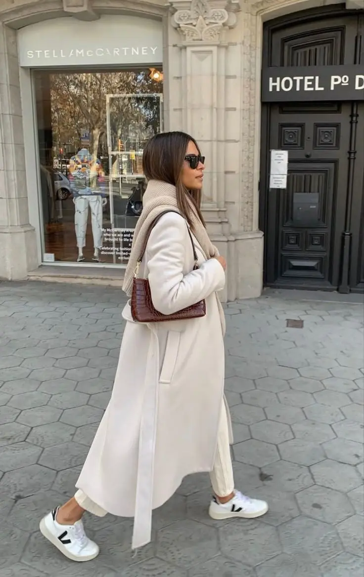 woman in long cream wool belted coat cream ribbed turtleneck ivory trousers brown croc embossed shoulder bag and white Veja sneakers outdoor street outfit 10