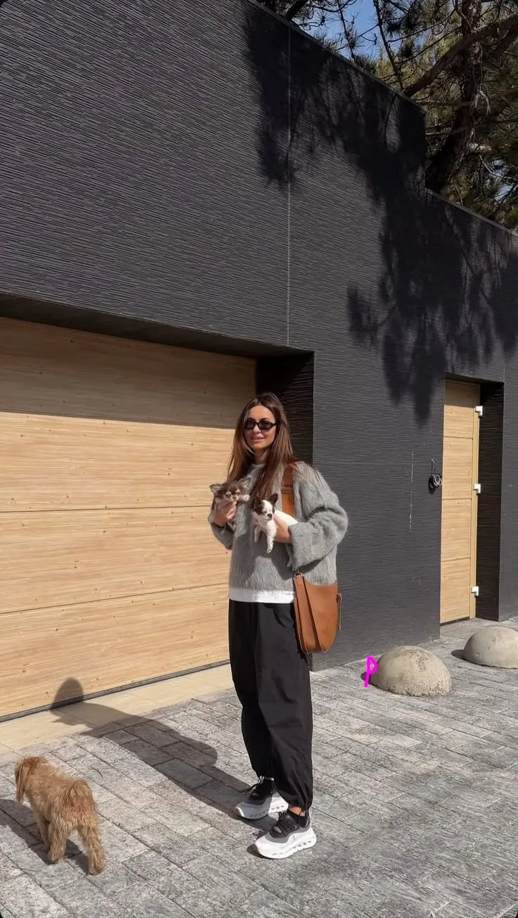 brunette woman outdoors holding small dogs in grey fuzzy oversized sweater white tee black relaxed trousers tan saddle shoulder bag black sunglasses On Cloud sneakers outfit 4