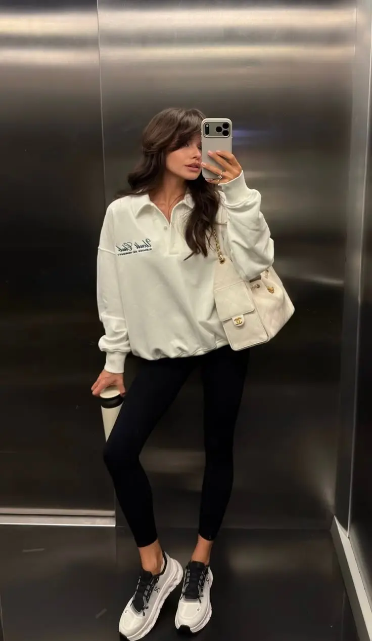 brunette woman in white polo collar oversized sweatshirt black leggings black and white On Cloud sneakers cream quilted shoulder bag elevator mirror selfie outfit 8