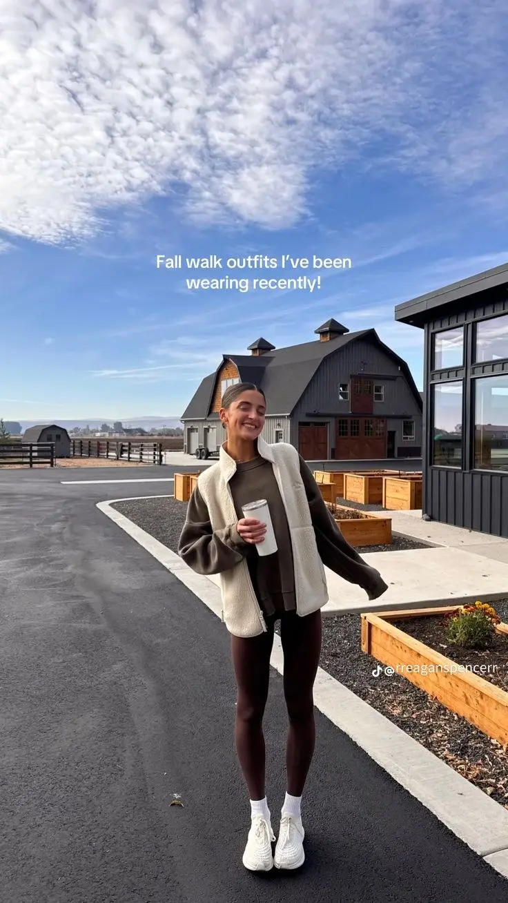 woman outdoors in cream sherpa vest over olive sweatshirt dark leggings white On Cloud sneakers holding coffee cup blue sky background outfit 11