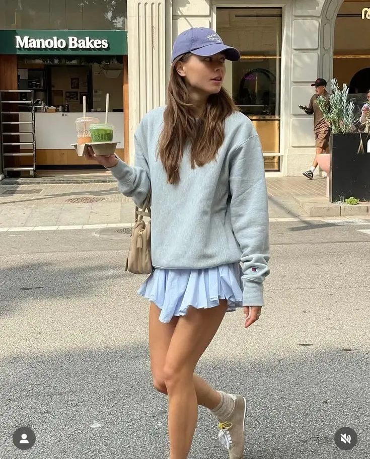 woman in grey Champion crewneck sweatshirt light blue pleated mini skirt lavender cap tan Alo sneakers white socks street outfit 2