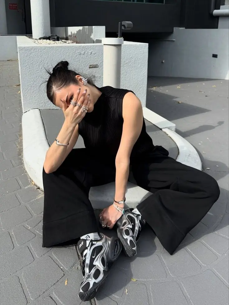 woman in black wide leg trousers black sleeveless ribbed top silver metallic chunky sneakers silver jewellery stacked rings outdoor sitting outfit 5
