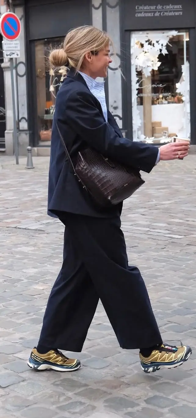 woman walking in navy wide leg blazer trousers suit light blue shirt chocolate croc bag gold detail trail sneakers cobblestone street outfit 6