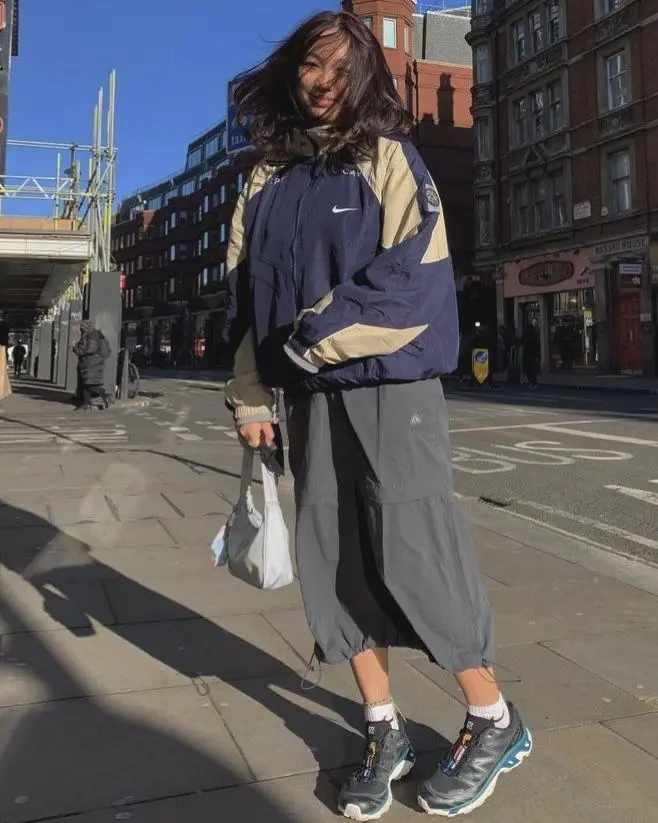 woman in oversized vintage nike colorblock windbreaker grey nylon midi skirt white socks salomon trail runners street outfit 7