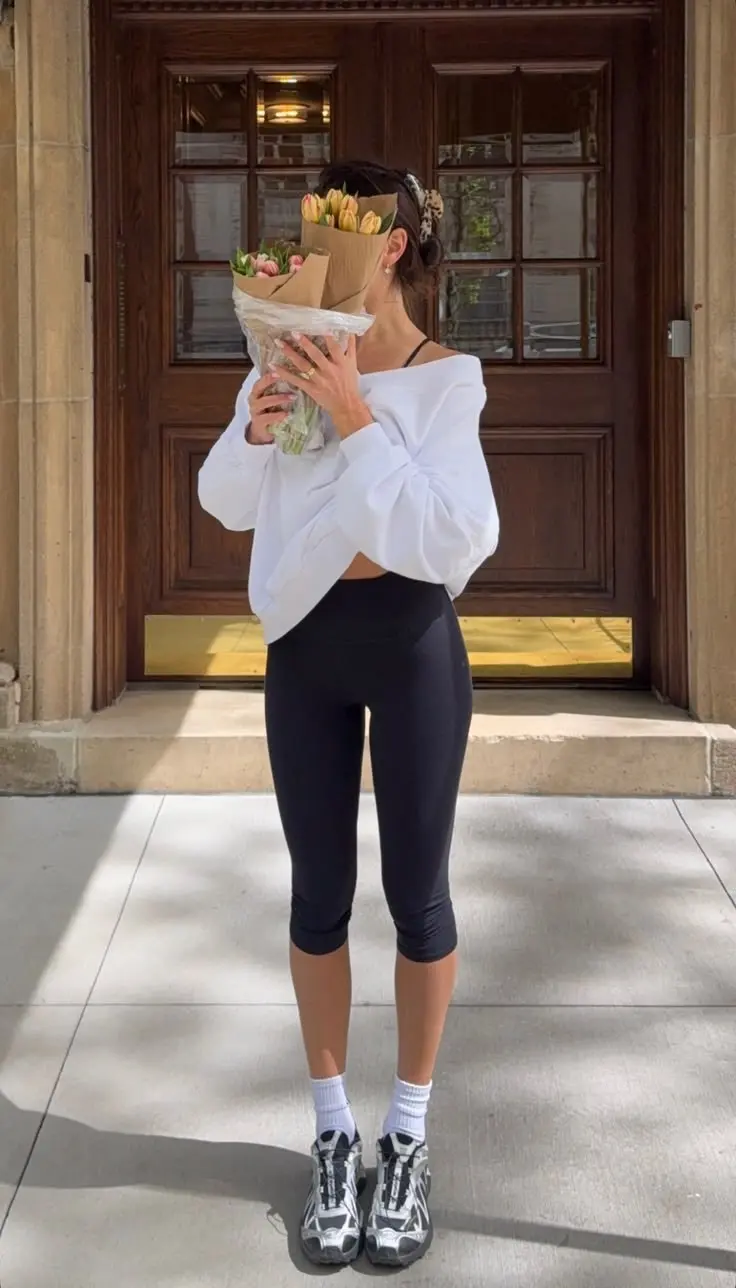 woman in white off shoulder sweatshirt black capri leggings white ankle socks silver chunky trail sneakers doorstep holding flowers outfit 8