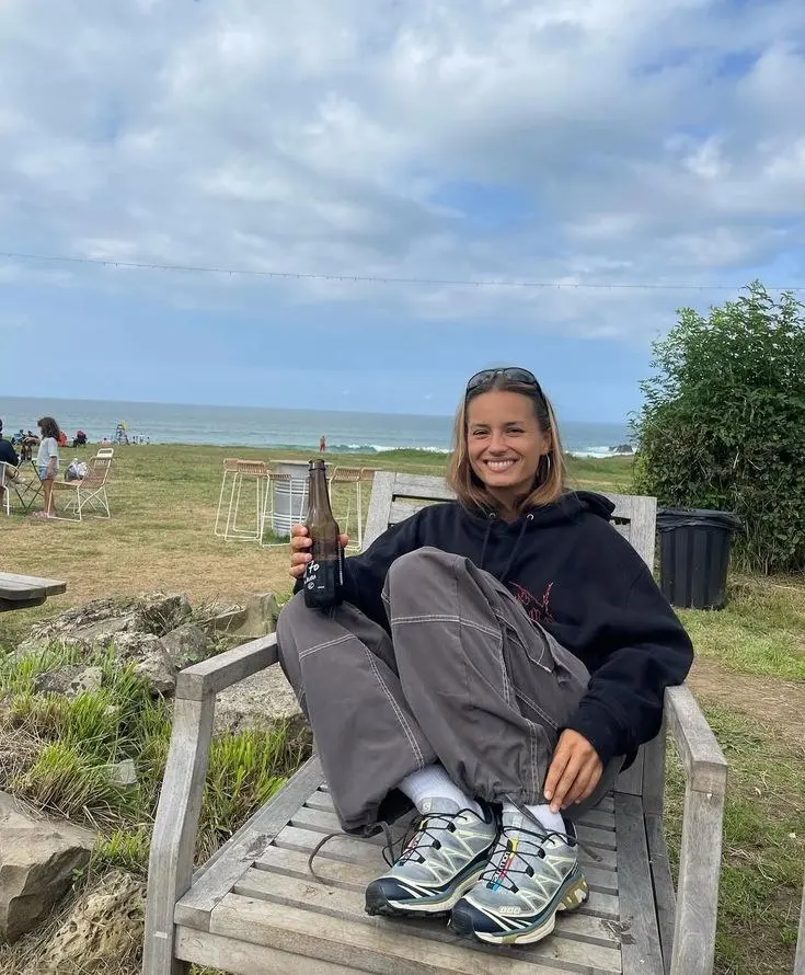 woman in black oversized hoodie grey cargo pants white socks light blue trail sneakers sitting outdoors near coast outfit 9