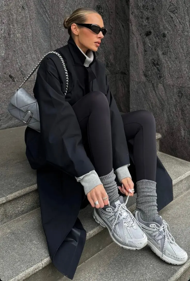 woman sitting on steps in black oversized structured coat grey turtleneck black leggings grey knee high socks silver grey new balance chunky sneakers grey quilted shoulder bag dark sunglasses outfit 19