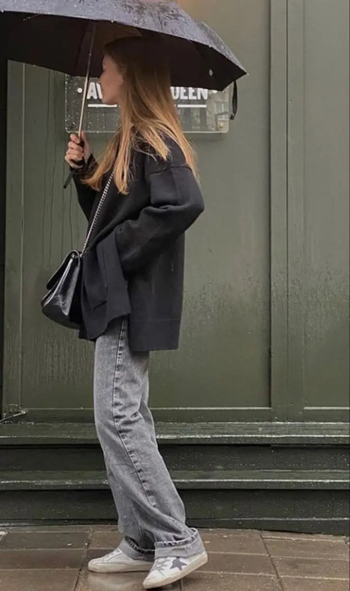 woman in oversized black blazer grey straight jeans black glossy shoulder bag white distressed sneakers rainy street photo 5