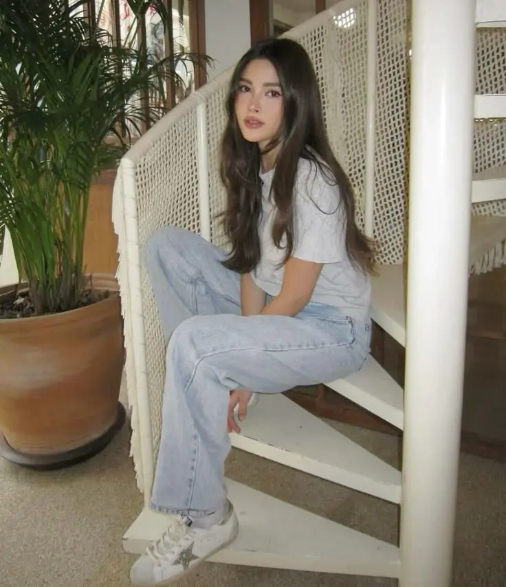 young woman in white crop tee light wash wide leg jeans white star sneakers sitting on white stairs indoor photo 6