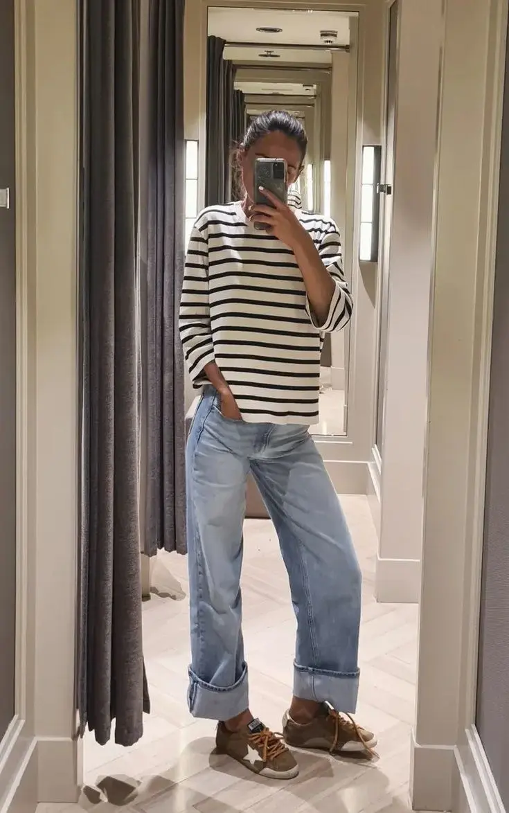 woman in navy white breton stripe long sleeve top light wash cuffed wide leg jeans olive brown distressed sneakers mirror selfie photo 12