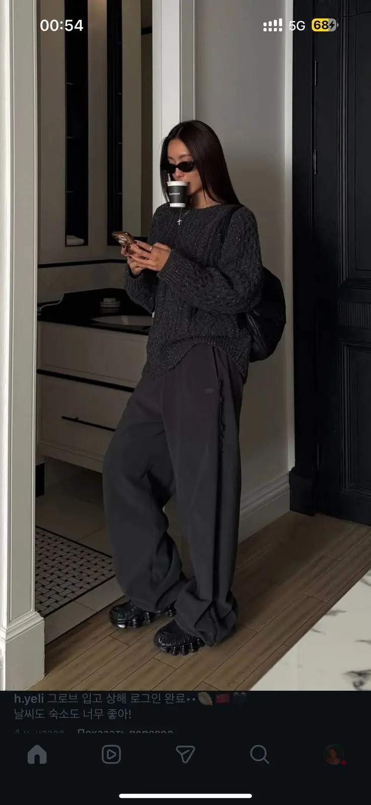 woman in dark charcoal cable knit oversized sweater charcoal wide leg high waist trousers black platform sole sneakers silver necklace small black sunglasses holding coffee indoor doorway outfit 3
