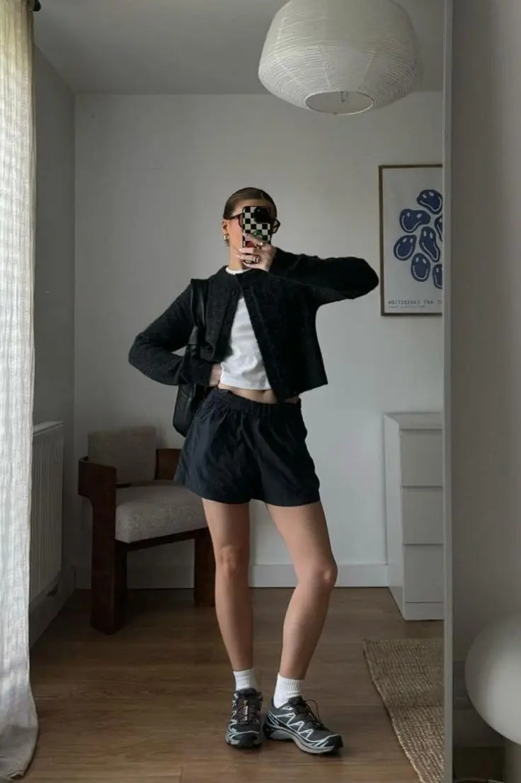 woman in dark charcoal textured button cardigan white crop tee black high waist athletic shorts black trail sneakers white socks small black crossbody bag checkered phone case mirror selfie outfit 8